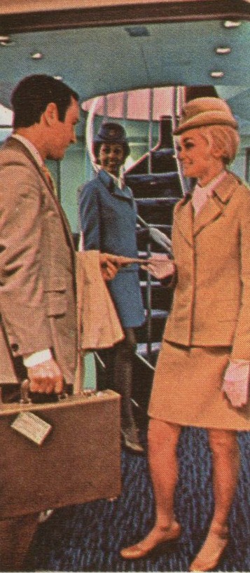 1970 A Flight Attendant wearing the 'Galaxy Gold' uniform greets customers in the doorway  of a mock up 747.